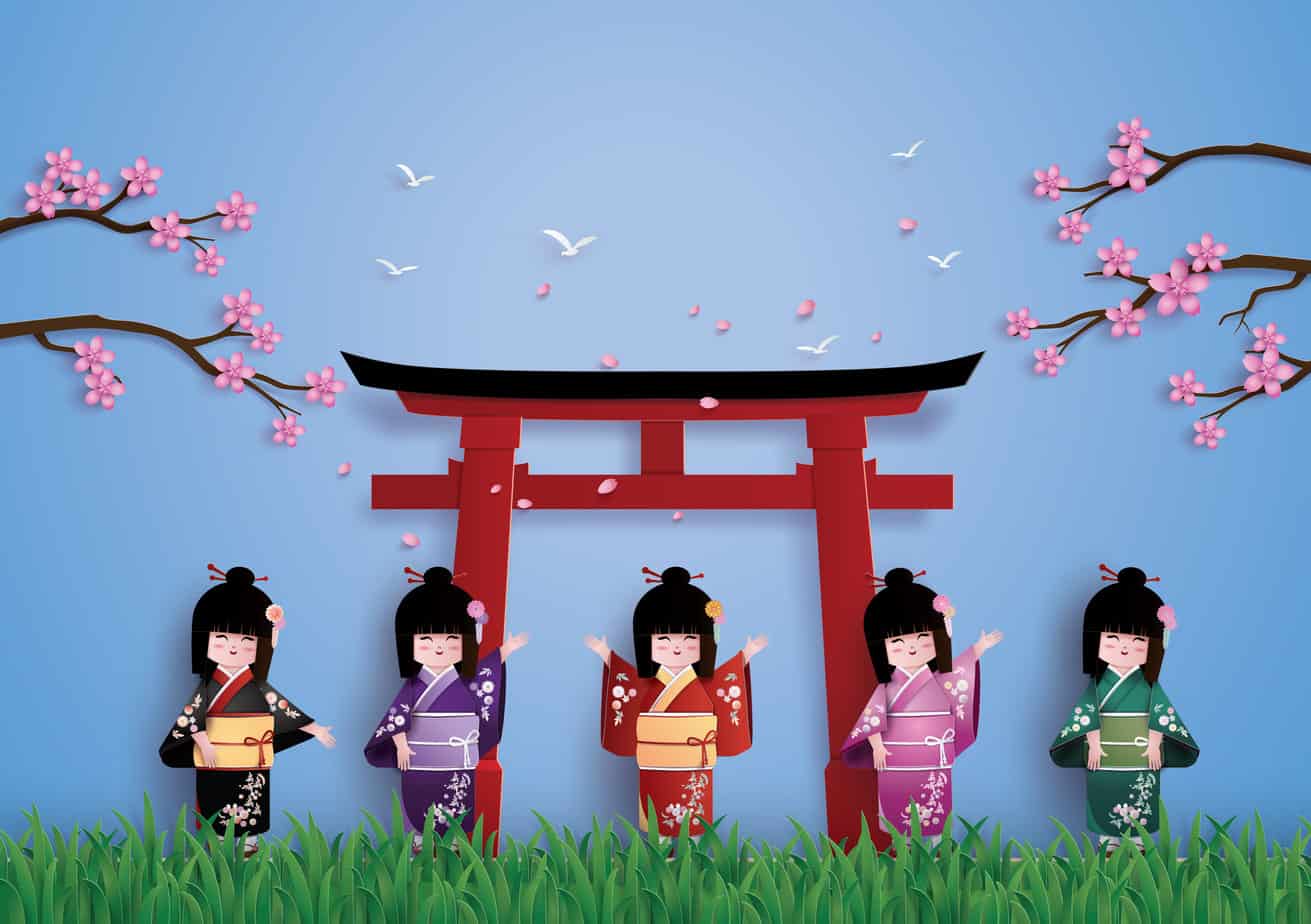 An image of a large, red, Japanese Toori gate in the background with sakura trees on either side of it and grass below. There are five Japanese girl dolls dressed in traditional Japanese clothes standing in a row and smiling in the foreground.