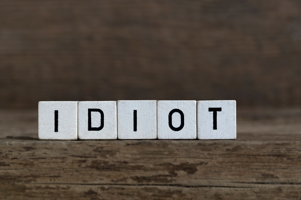 An image of five, small white cubs with letters on them. Them are placed side-by-side on top of a wooden surface. The words spell out the word, “IDIOT.”