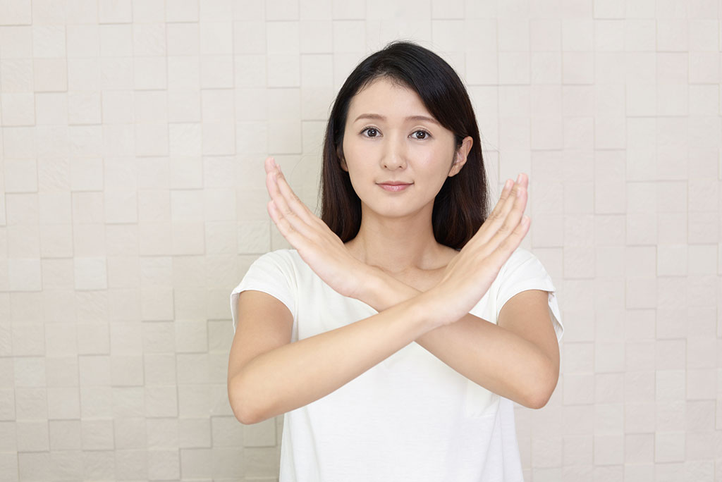 A young Asian woman is crossing her arms in front of her to form an “X,” the gestures for “no” or “no good” in Japanese.
