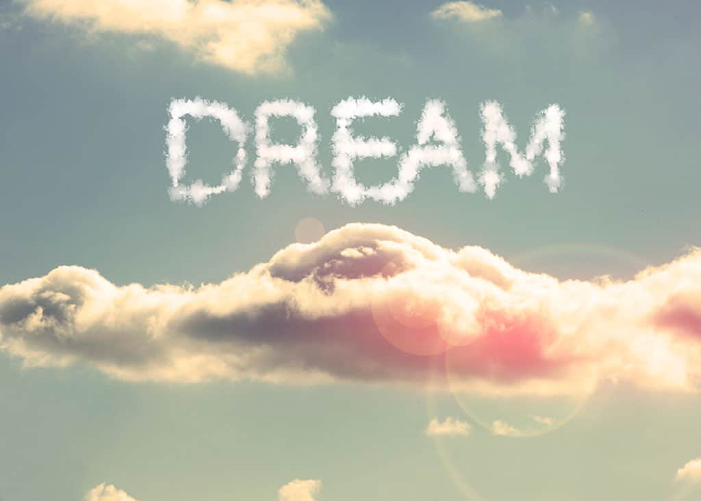 An illustration of clouds in the blue sky. There is a big cloud in the middle of the image. Above it, is the word “DREAM” spelled out in a whitish, cloud-shaped font.