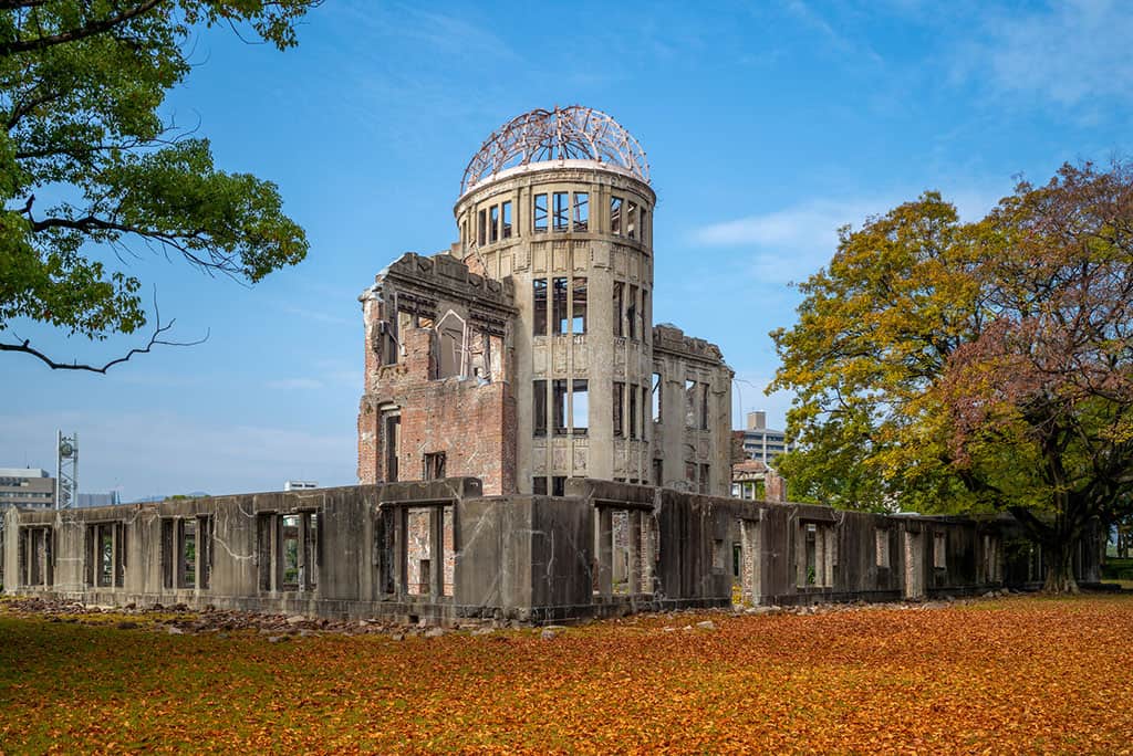 The Atomic Bomb Dome in Hiroshima, Japan with trees around it and yellow leaves on the ground.