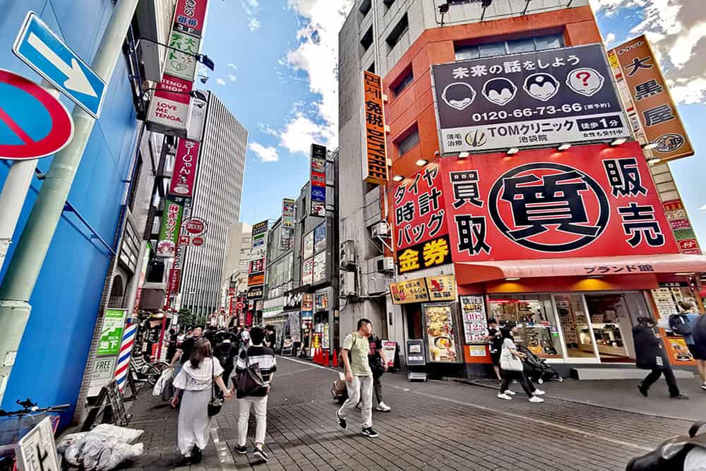 A street in Ikebukuro, Tokyo with people walking down the streets and a lot of signs on the surrounding buildings.