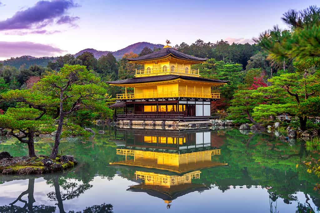 Kinkaku-ji (The Golden Pavilion) reflecting on a pond in front of it with green trees around it.