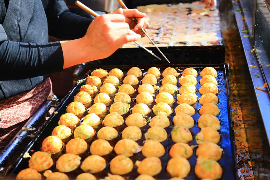 A close-up of someone making takoyaki (octopus balls) on a takoyaki grill.